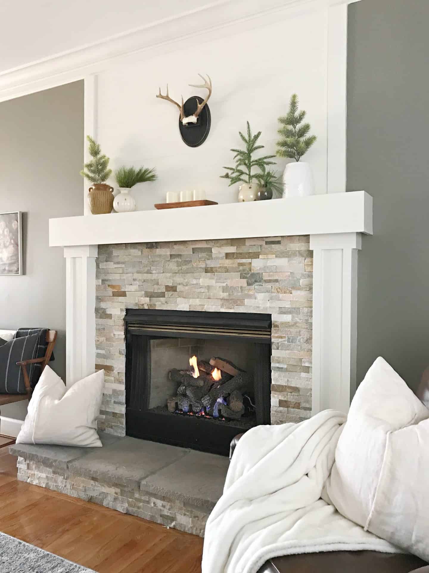 Stone Fireplace Mantel Adorned with Faux Evergreen Trees and Deer Head — Winter Decor After Christmas