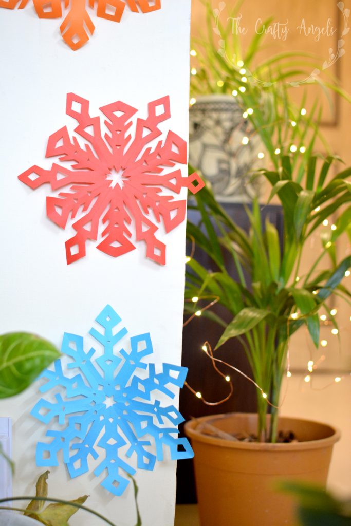 Colorful Paper Snowflakes on a White Wall With Fairy Lights