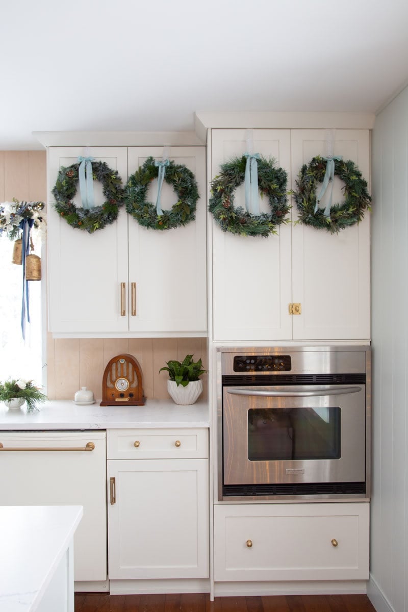 White Farmhouse Cabinets with Green Wreaths and Blue Ribbons — Farmhouse Christmas Kitchen