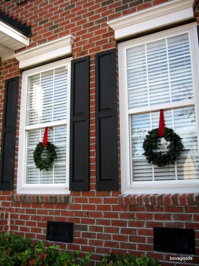 Symmetrical Green Wreaths with Red Ribbons on Brick House Windows — Christmas Window Decor Outdoor
