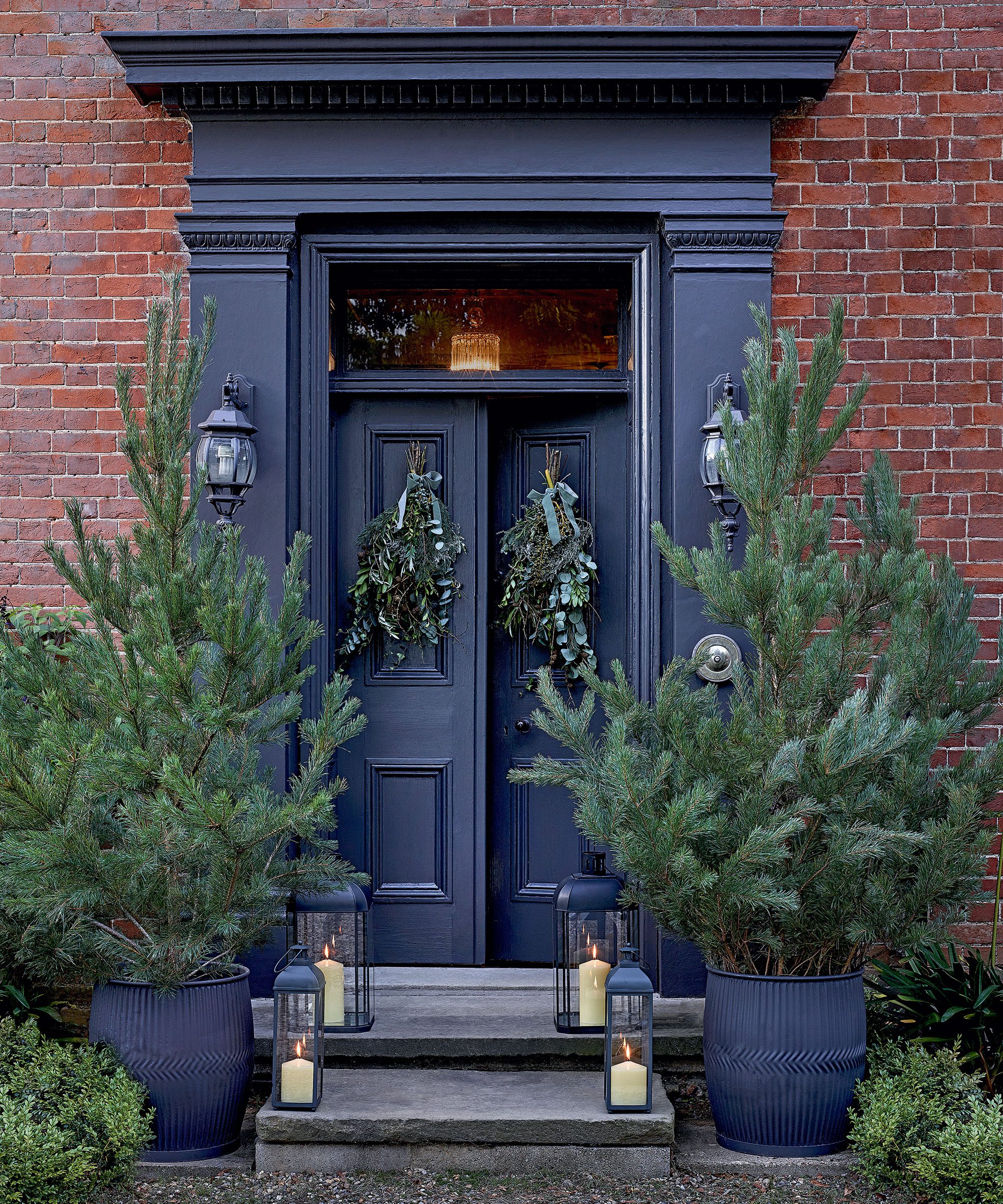 Dark Blue Double Doors Against Red Brick with Pine Trees and Lanterns Dark Blue Double Doors Against Red Brick with Pine Trees and Lanterns — Christmas Front Door Decor