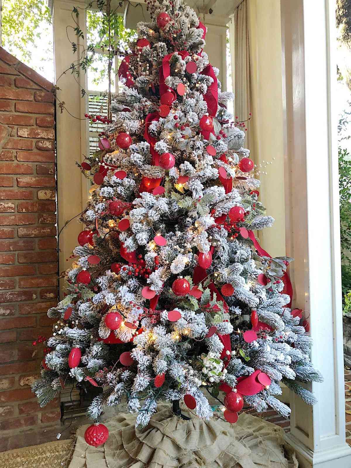 Traditional Flocked Christmas Tree with Abundant Red Ribbon and Ornaments on a Porch — Vertical Ribbon Christmas Tree