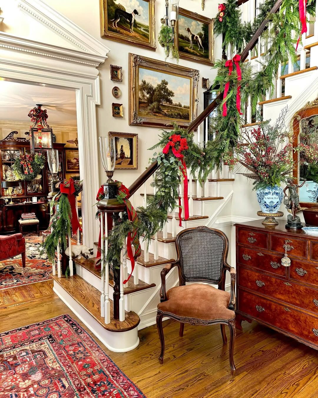 Traditional Staircase with Abundant Garland, Red Bows, and Antique Furniture Traditional Staircase with Abundant Garland, Red Bows, and Antique Furniture — Christmas Staircase Decor
