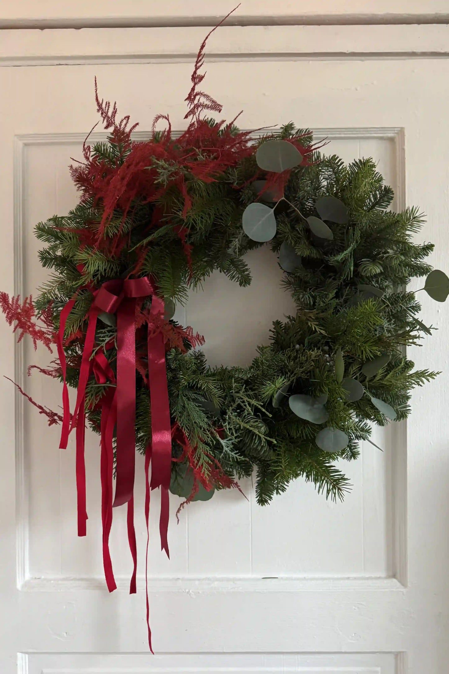 Traditional Wreath with Burgundy Ribbons on a White Door Traditional Wreath with Burgundy Ribbons on a White Door — Burgundy Christmas Decor
